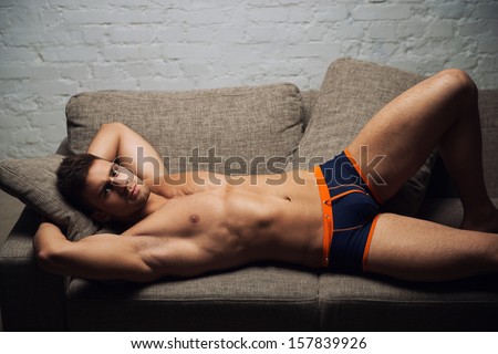 Naked male model lying on sofa on white wall background