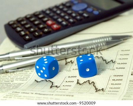 Calculator pens dice and financial pages of a newspaper.