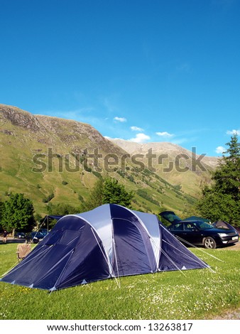 Blue family tent in camping ground with mountains behind and clear blue sky
