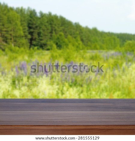 Empty wooden table. In the background is blurred green meadow