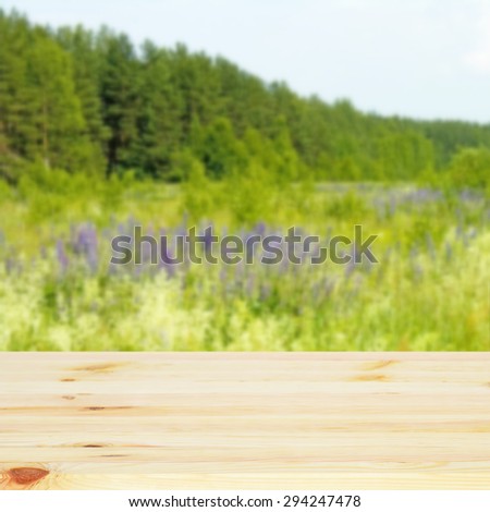Empty wooden table. In the background is blurred green meadow