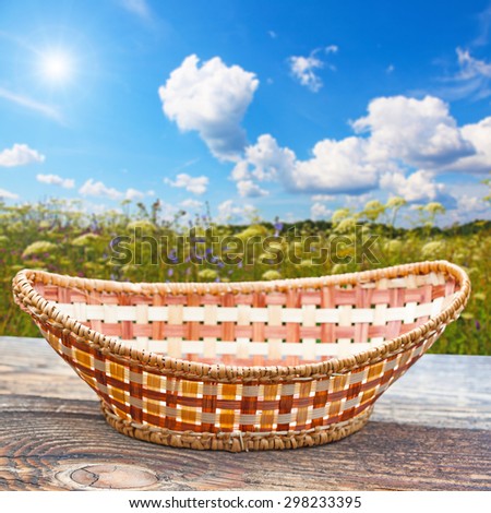 Empty basket on old wooden table.In the background blurred beautiful field with wild flowers