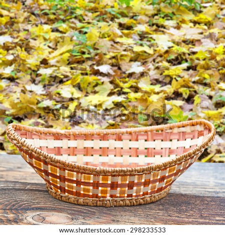 Empty basket on old wooden table.In the background blurred autumn leaves