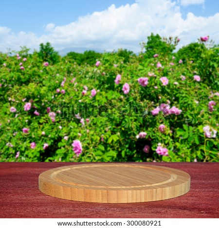 Empty round cutting board on wooden table.Blurred rose field in the background