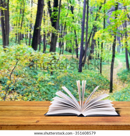 Open book on a rustic wooden table. In the background autumn trees in the park
