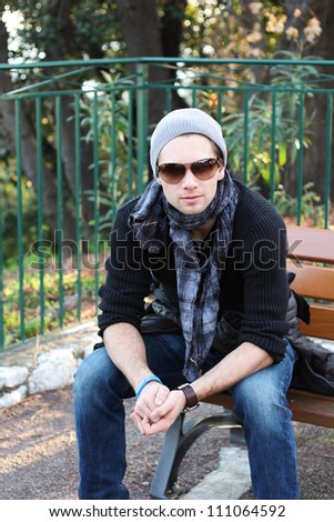 Young stylish man with scarf and beanie sitting on a bench