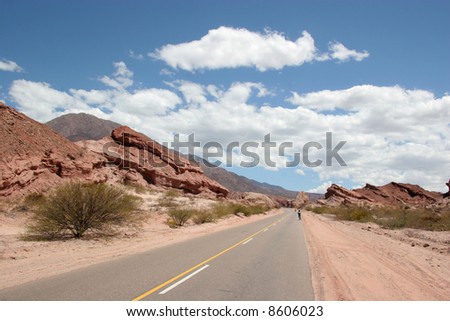 A lonely desert road with a few bicycle riders in the distance