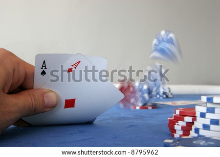 A poker player holds two aces and throws chips onto the table to place a bet