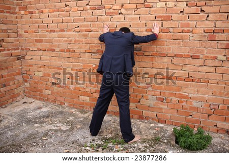 A man in a suit is standing with the head down against a brick wall