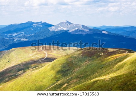 View of green mountain with meadow, blue mountains away and blue sky.
