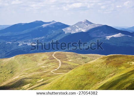 View of green mountain with meadow, blue mountains away and sky.
