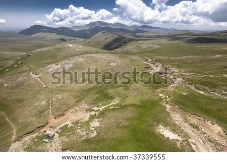Aerial view of grassland in mountains. Mountains in the back, cloudy sky.