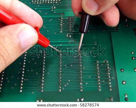 Technician holding test leads troubleshooting a printed circuit board.