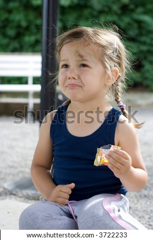 little girl sitting on the ground and eating candy