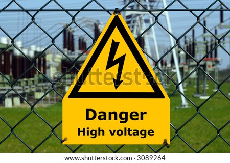 USA high voltage sign with substation, blue sky and green grass in the background.