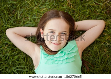 A young girl is lying on her back on the green grass smiling.