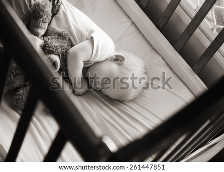sweet baby sleeping in his crib with his teddy bear in black and white