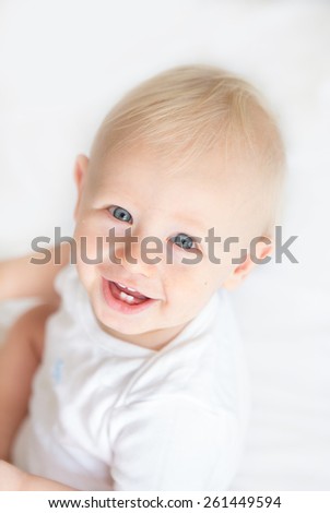 A happy baby boy with blond hair and blue eyes smiling up at the camera against a white background