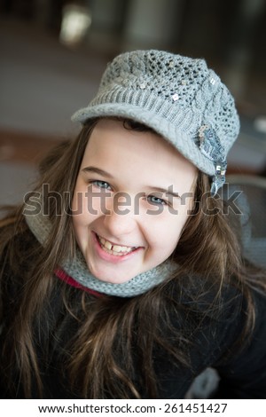 A attractive young tween dressed in winter coat and wool hat smiles at the camera.