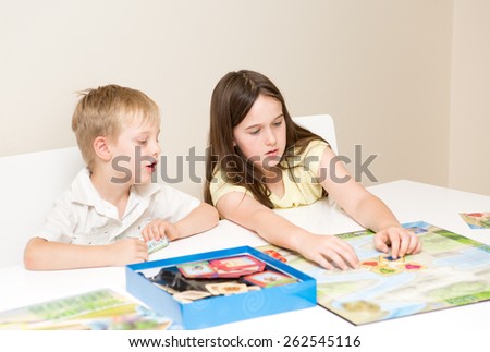 Siblings, a boy and girl play a board game on a white table against a white background