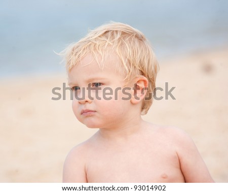 A little boy with a serious expression on the beach glances sideways.