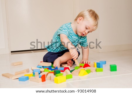 A little 15 month old boy playing with colorful blocks indoors.
