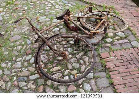 Rusty old bicycle, apparently just fished out of a canal, lying on cobble-stones