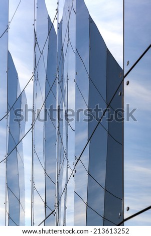 glass panes on facade of trade building reflecting blue sky and another building