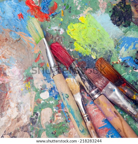 colorful palette full of paint spots and paint brushes