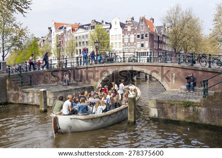 Amsterdam, Netherlands, 10 May 2015: open boat full of young people enters Prinsengracht under bridge in Amsterdam canal on sunny spring day
