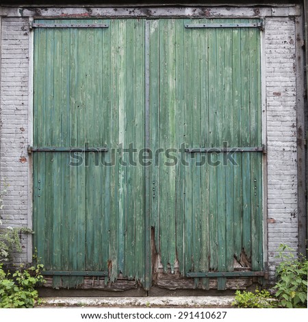large old barn doors with peeling green paint in white brick wall