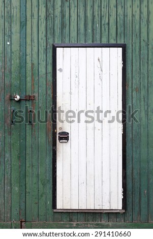 small white door in large green barn door with peeling green paint