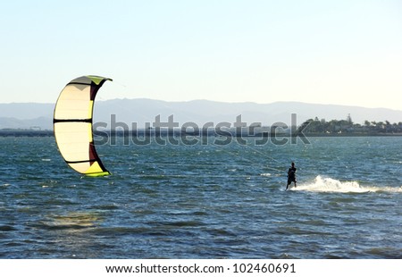 Kite surfer speeding across the water at sunset.