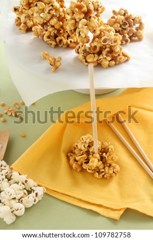 Caramel popcorn on a stick with raw popcorn on the side.