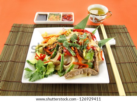 Freshly prepared beef noodle stirfry with condiments and green tea.