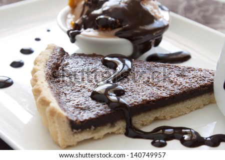 Chocolate tart slice and ice cream with melted dripping chocolate sauce.