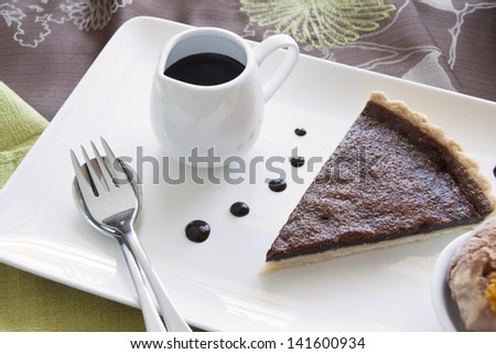 Delicious slice of chocolate tart with jug of chocolate sauce.