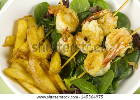 Yummy fried shrimp skewers with chunky chips on a salad ready to serve.