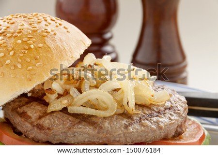 Freshly cooked hamburger with fried onions and a sesame seed roll.