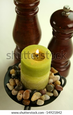 Salt and pepper grinders with a candle set in stones with subdued lighting.
