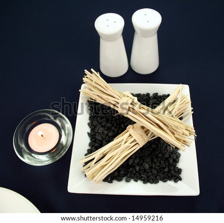 Salt and pepper grinders with a candle and cane decoration set in stones with subdued lighting.