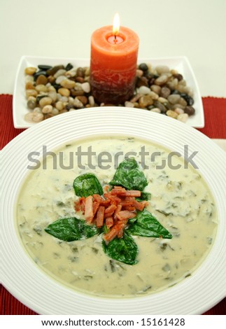 Creamy spinach soup with crispy bacon and spinach leaves with candle.