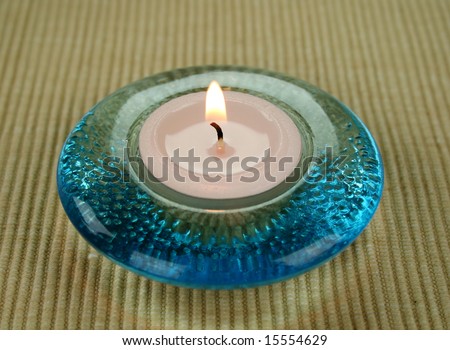 Burning tea candle in a round blue glass candle holder.