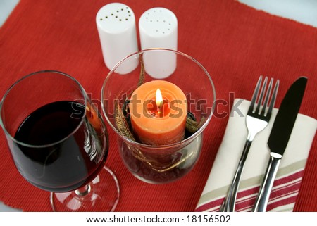 Dinner decor with an ornate candle, cutlery, salt and pepper shakers and a glass of red wine.