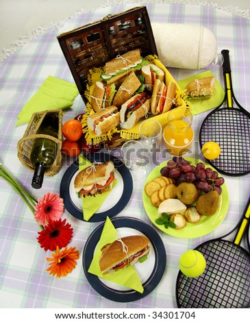 Selection of food for a picnic with a hamper, basket, fruit, wine and tennis racquets.
