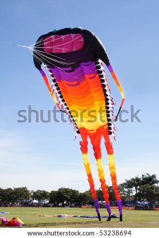 Giant colorful kite in the shape of a long catapillar like creature leaving the ground.
