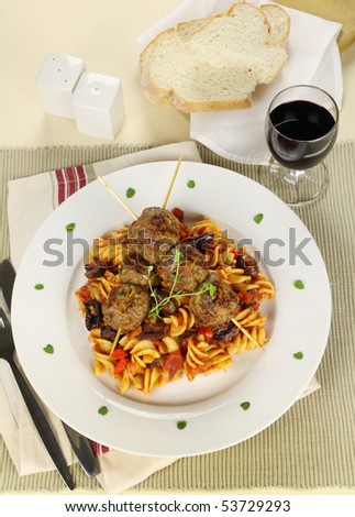 Delicious beef meatballs on tomato and olive pasta with bread and wine.