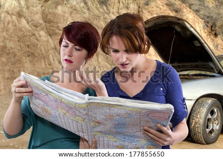 two young women are lost and looking at a map. broken car in the background
