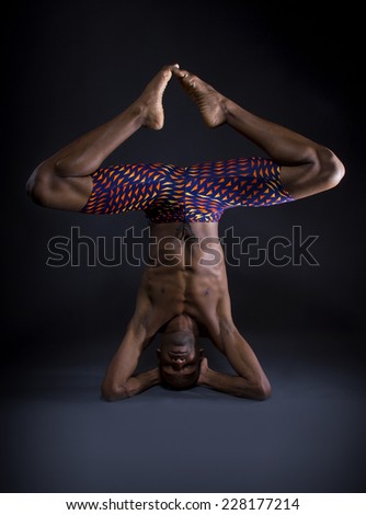 muscular black man doing upside down yoga on grey background