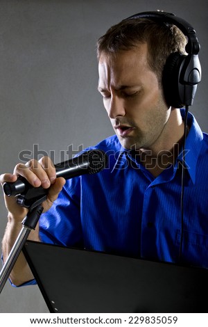 male voice over artist or singer on a microphone wearing a blue shirt on a concrete background